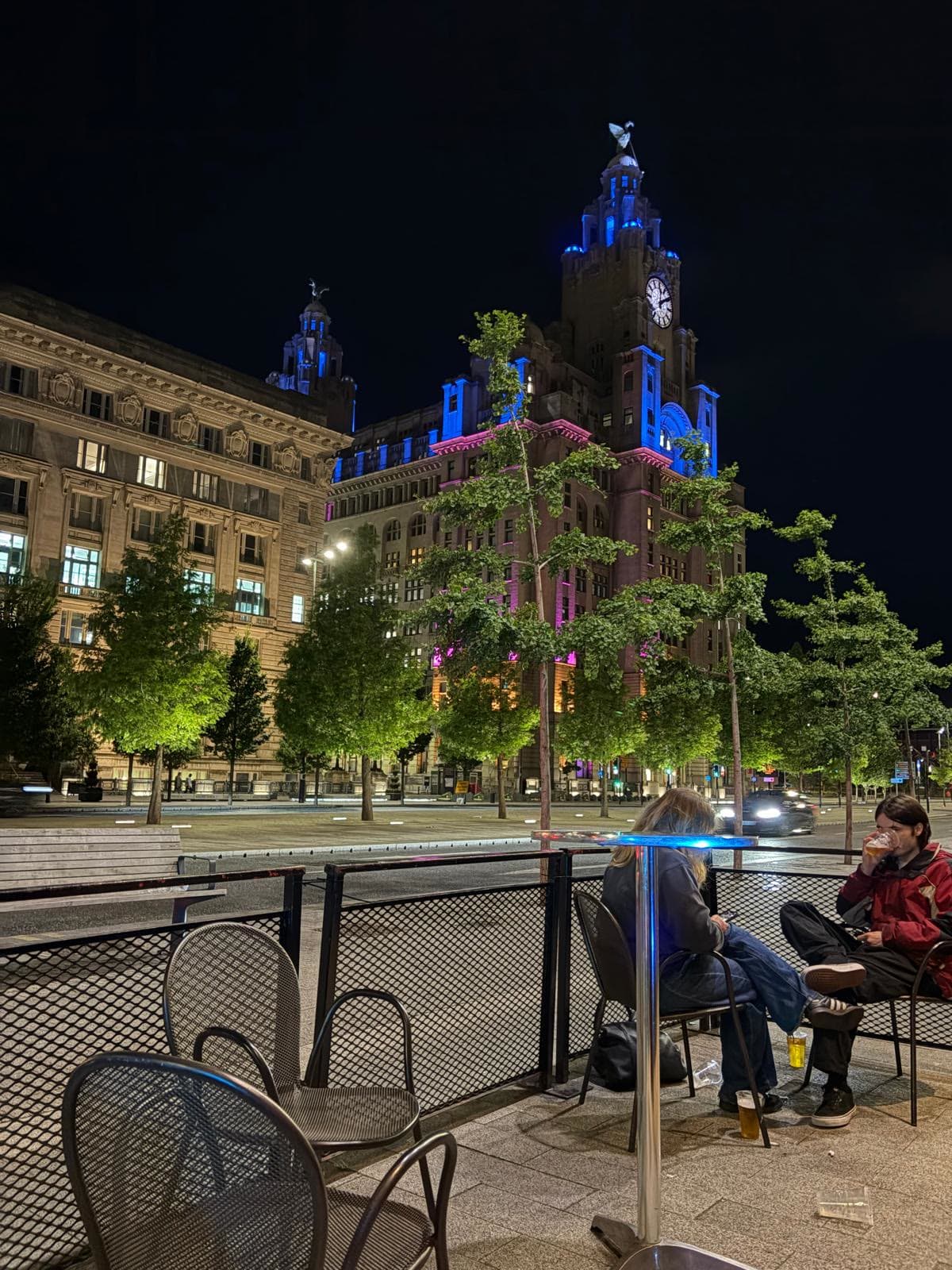 The Royal Liver Building lit up at night, photographed from the seating outside Gracy's