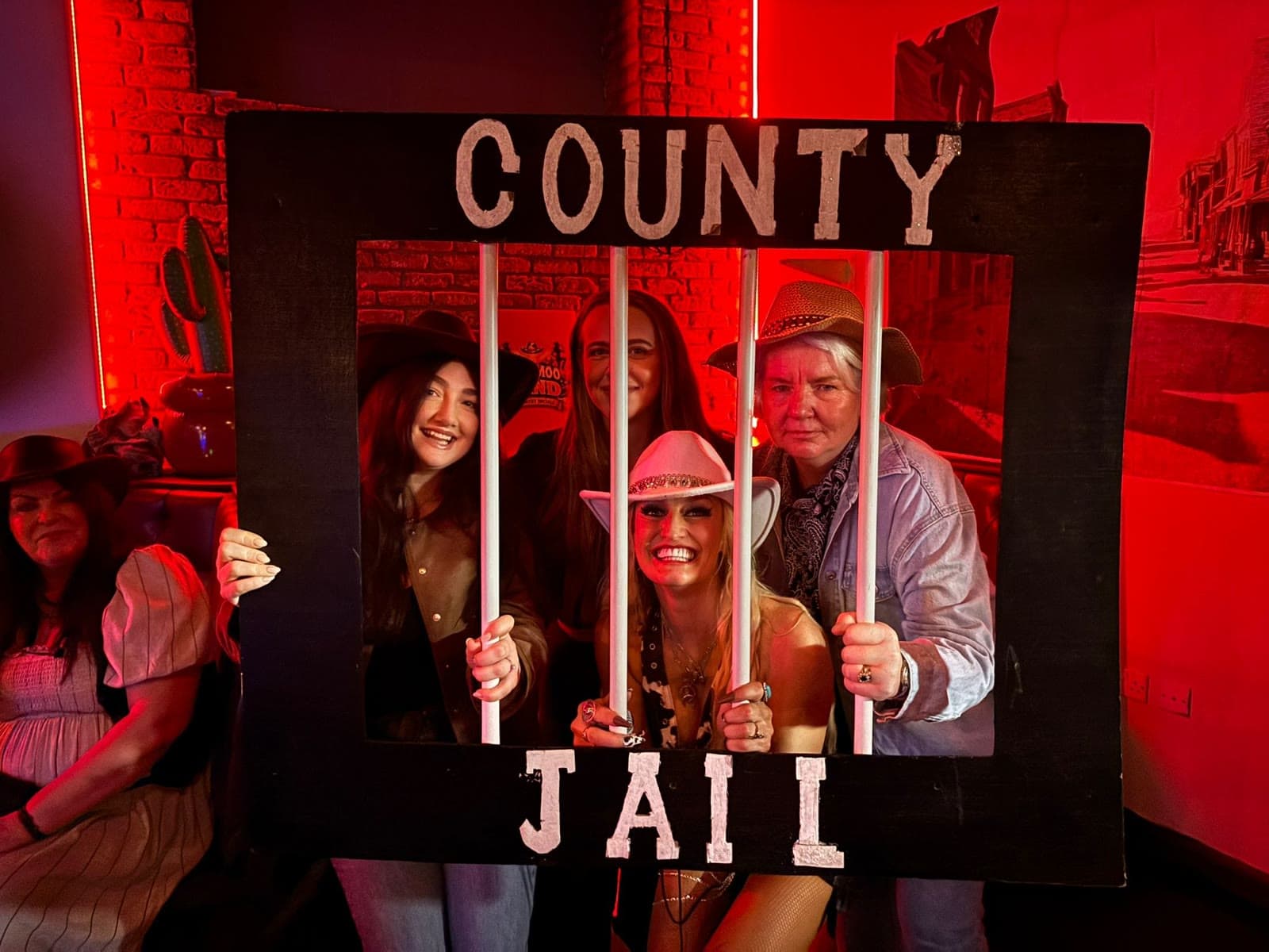 Guests in cowboy hats behind a County Jail photo frame at a country social at Gracy's